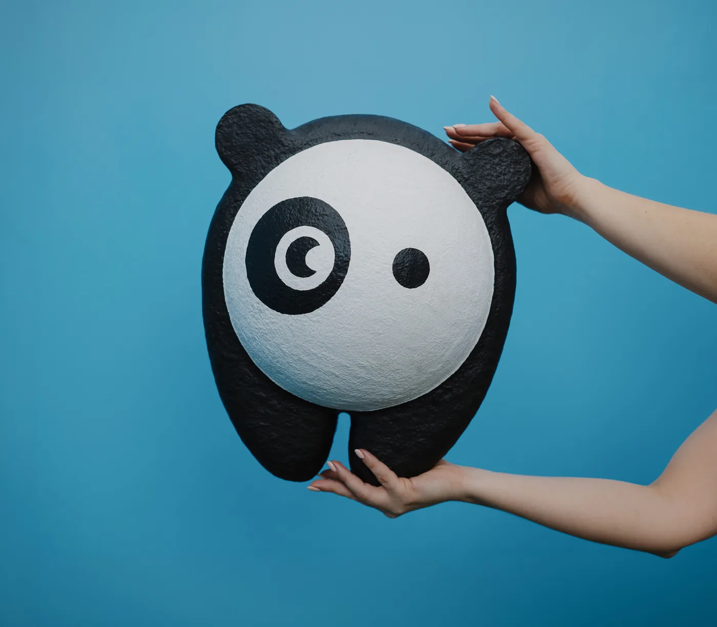 Two hands holding up a giant Bored Panda mask against a blue wall