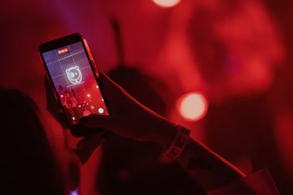 A fan filming a Bored Panda show on their phone in red stage light